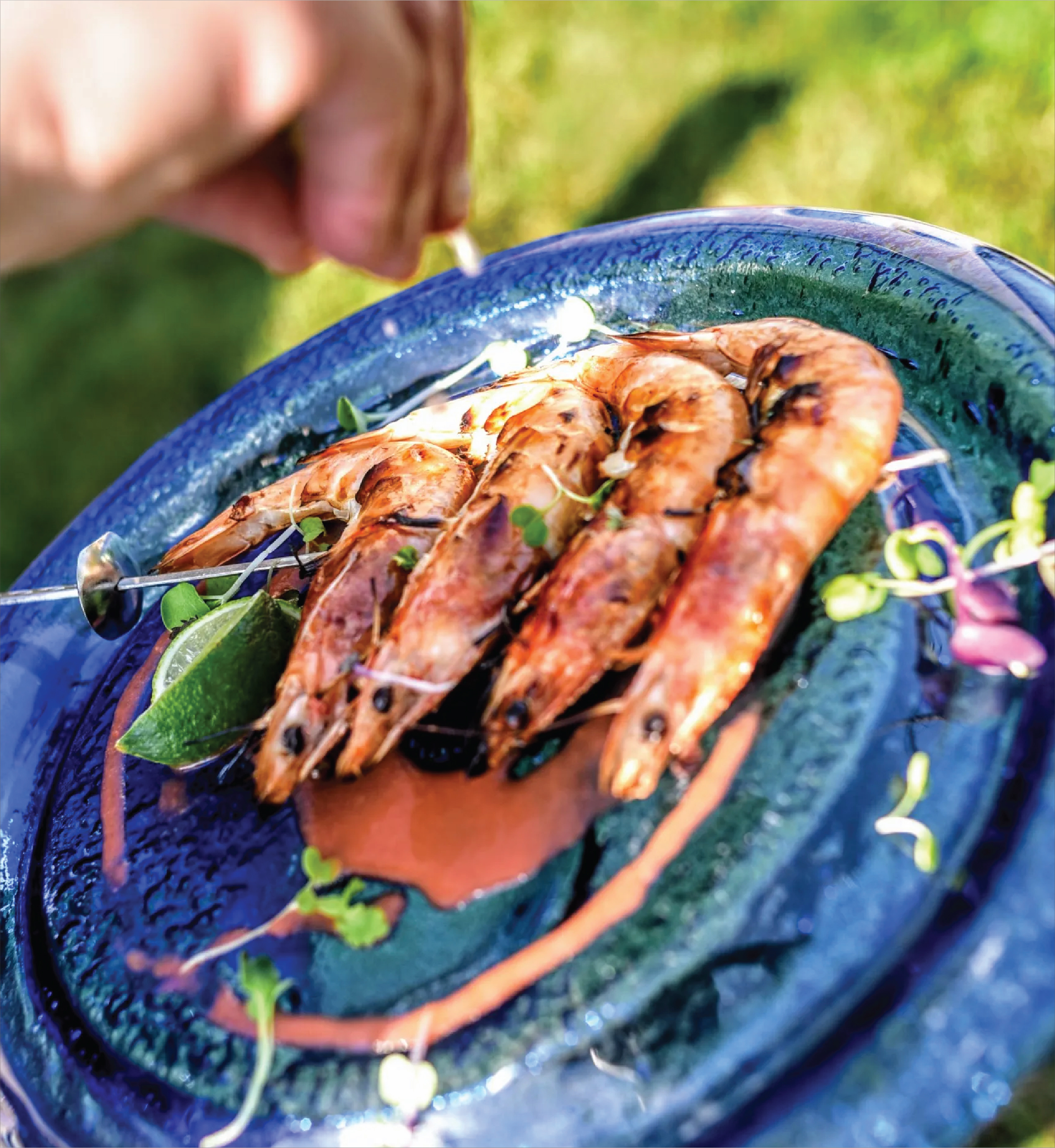 Grilled shrimp skewers garnished with lime and herbs on a blue plate