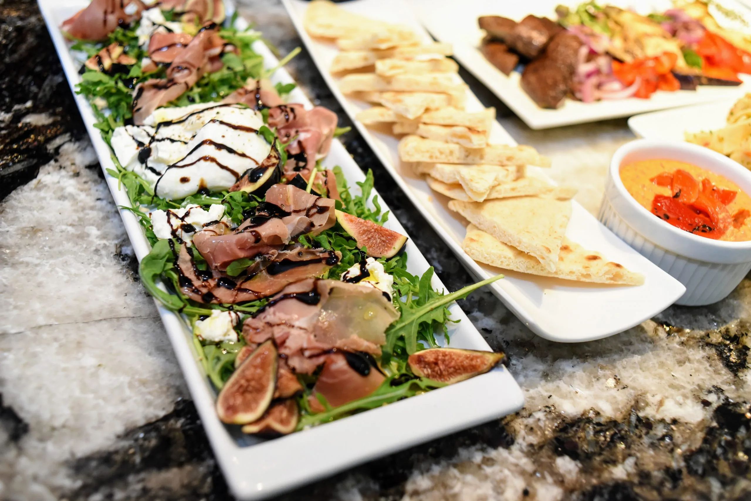 Platter of prosciutto, figs, arugula, and fresh cheese drizzled with balsamic glaze